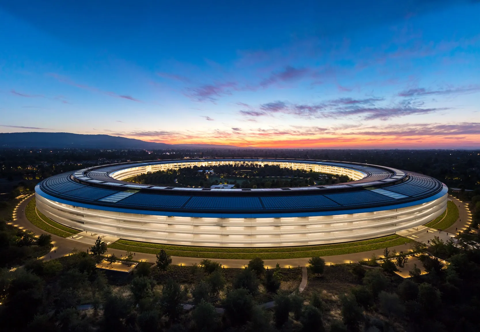 Ring HQ from above at golden hour, lit glass façade against the hills.