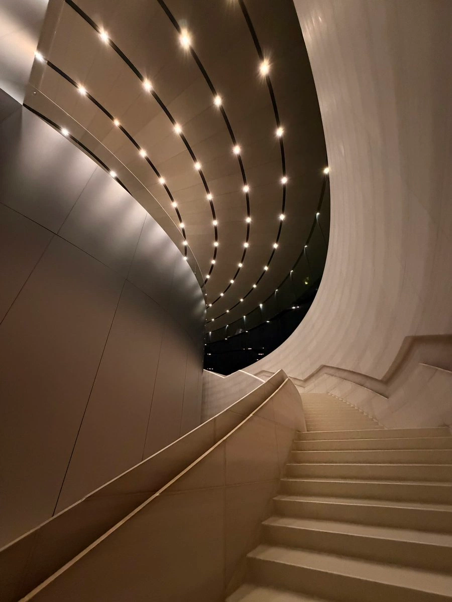 Curved stairwell, layered light bands wrapping the white walls.