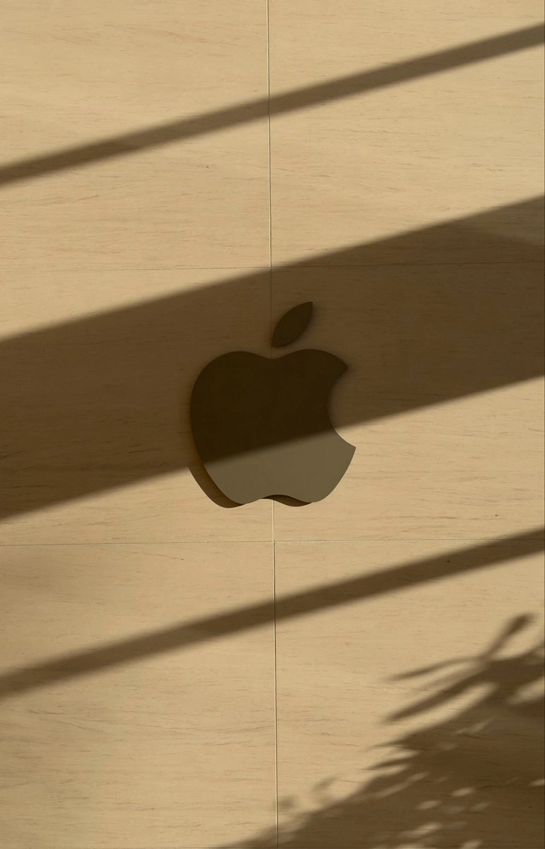 Apple mark cut into warm wood, soft shadow lines across the wall.